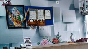 A reception desk with a framed religious painting, a bulletin board with notices, and a peacock statue. - Amrit Hotel & Resort (Thanagazi)