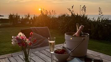 A wooden table with a glass of champagne, a bowl of strawberries, a book, and a bucket with a bottle and glasses.