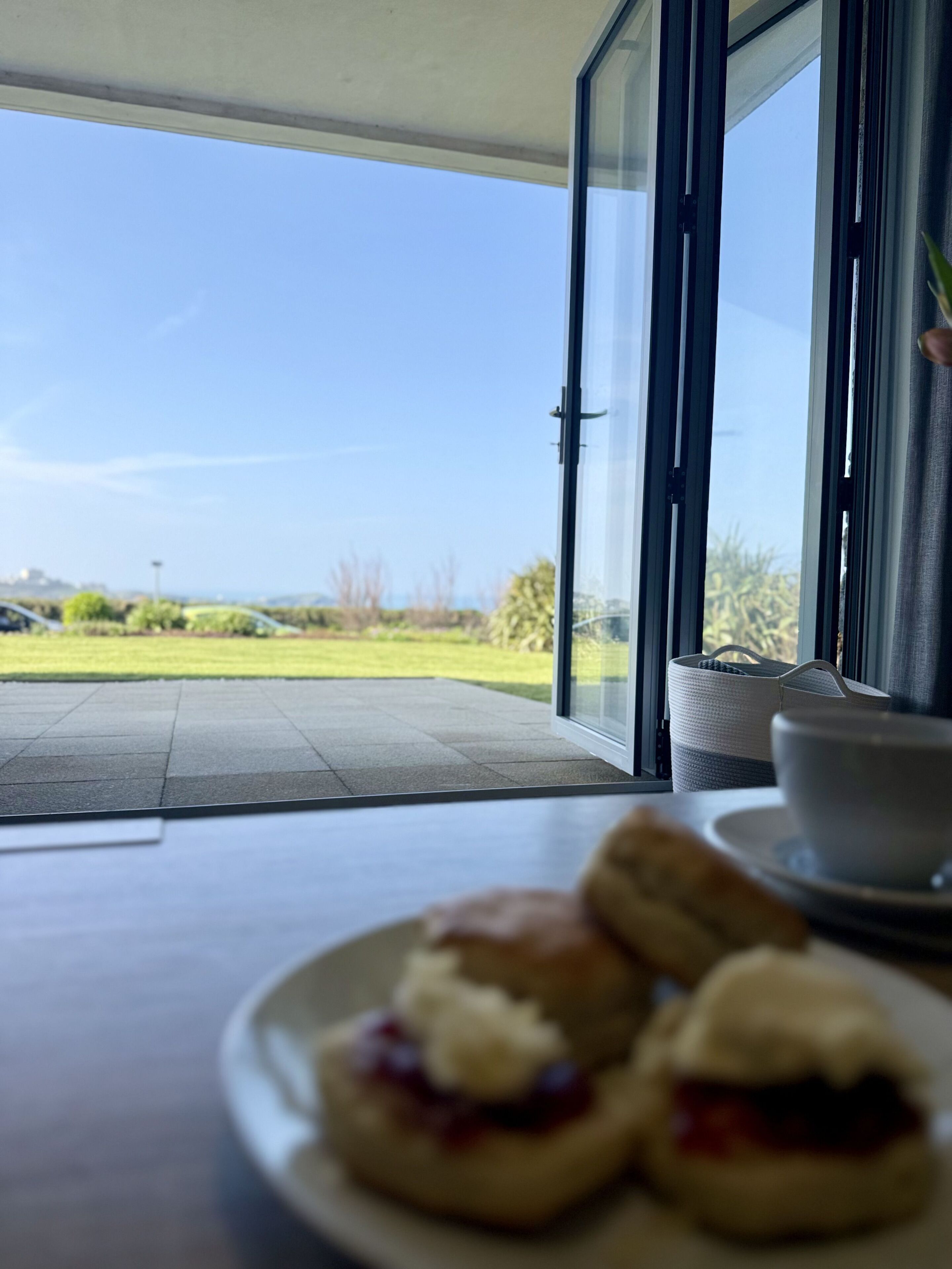 A dining area with a view of the outdoors, a table with a plate of scones, and a basket.