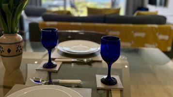 A dining table set with plates, cutlery, and blue glassware, with a view of a modern living area in the background.