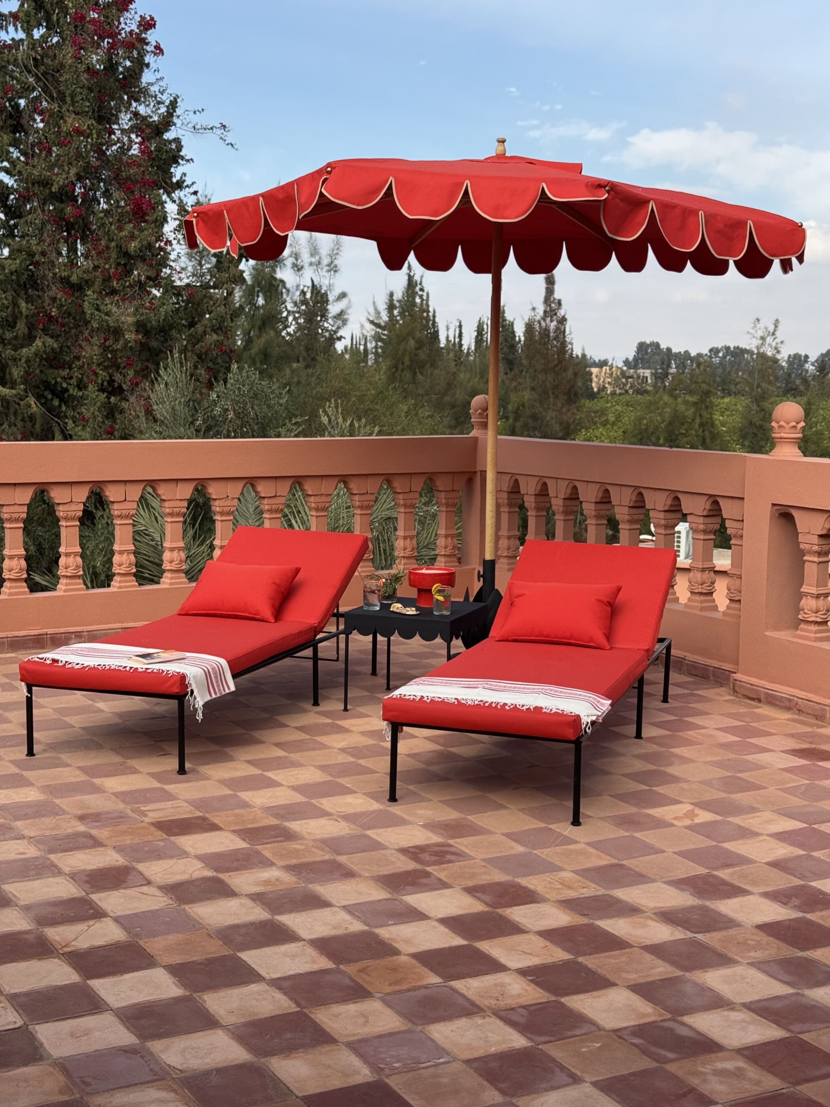 A terrace with two red lounge chairs, a red umbrella, and a checkered floor.