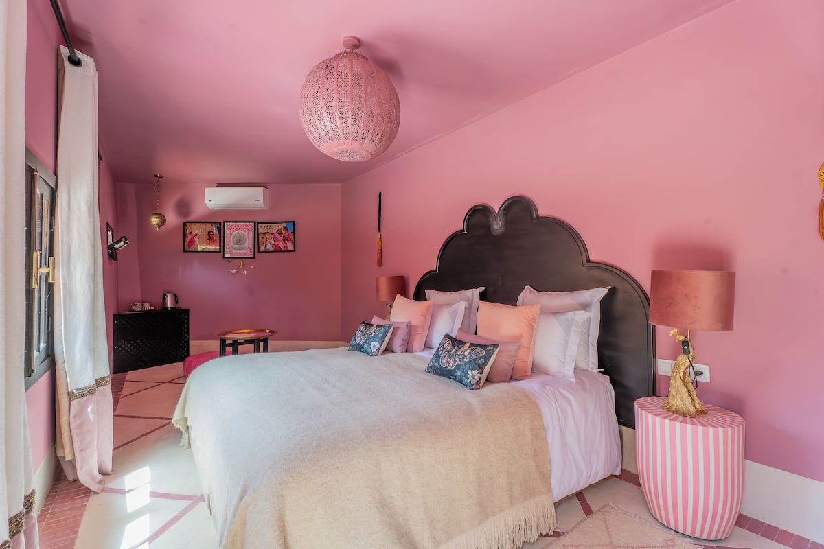 A pink-themed bedroom with a bed, bedside lamps, and a decorative wall hanging.