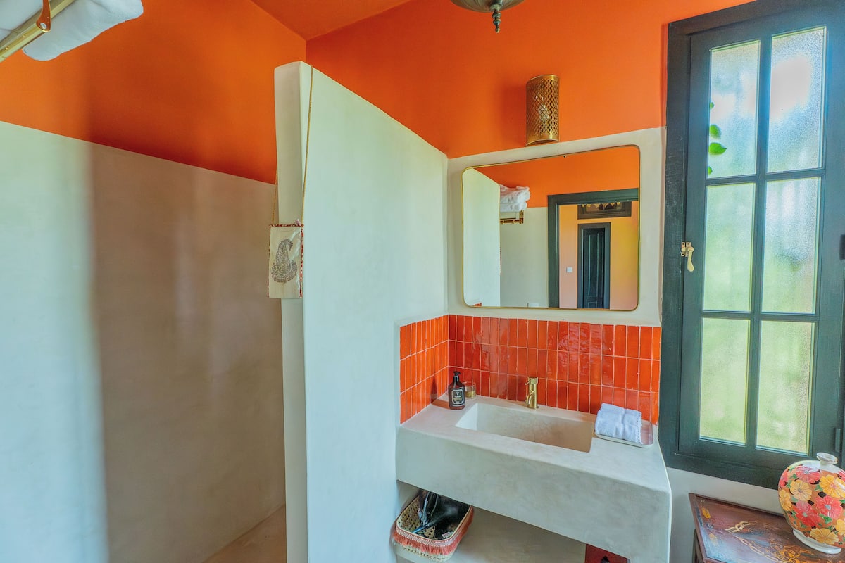A bathroom with a white sink, orange tiles, a mirror, and a window with a view.