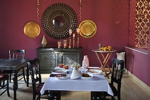 Een eethoek met een tafel voor vier personen, een kast met decoratieve objecten, en een muur met een decoratieve spiegel en twee wanddecoraties.
