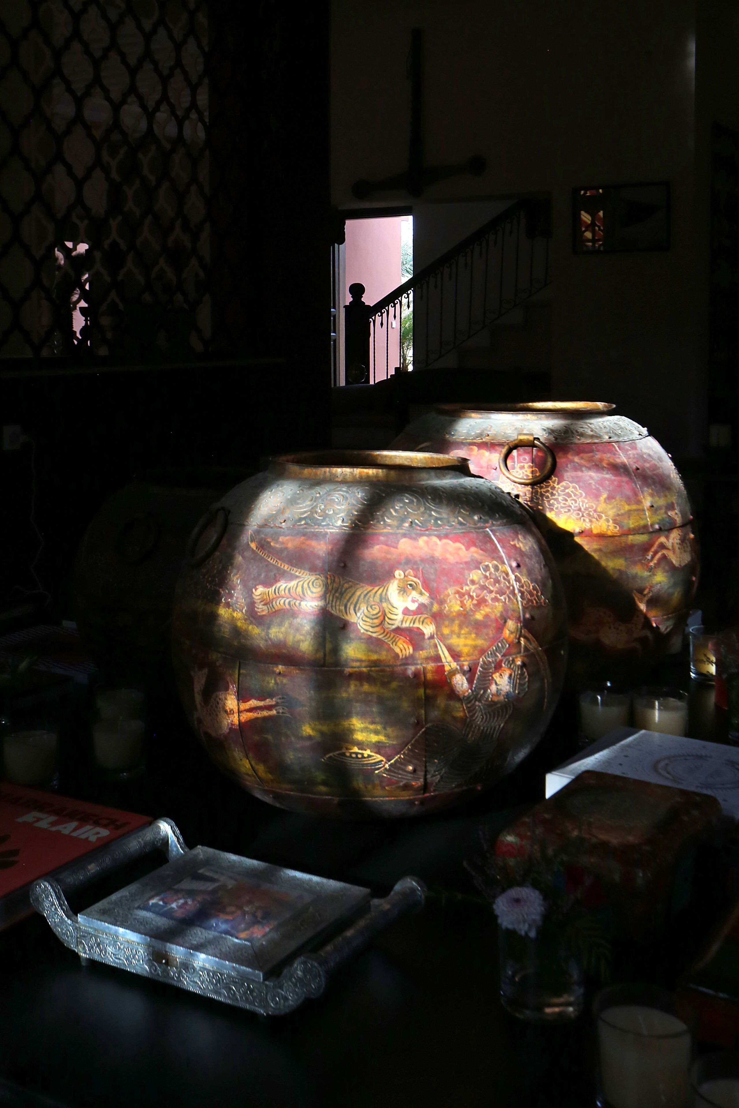 A dimly lit room with a large decorative metal object, a staircase, and a small table with a tray.