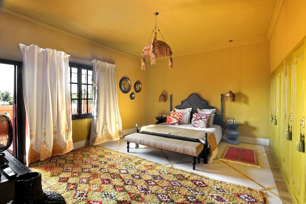 A bedroom with a bed, curtains, a patterned rug, a chandelier, and a wardrobe.