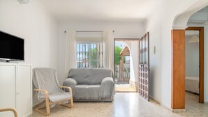 A hallway with a grey sofa, a wooden chair, a television on a cabinet, and a view of the outside. - Holiday Home 'Diego' with Private Garden and Wi-Fi (Vejer de la Frontera)