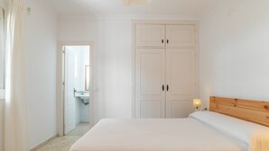 A bedroom with a bed, a wardrobe, a nightstand with a lamp, and a bathroom visible through an open door. - Holiday Home 'Diego' with Private Garden and Wi-Fi (Vejer de la Frontera)