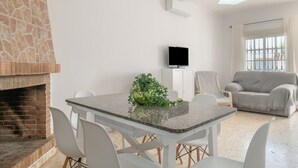 A living room with a stone fireplace, a dining table with chairs, a grey sofa, and a television on the wall. - Holiday Home 'Diego' with Private Garden and Wi-Fi (Vejer de la Frontera)