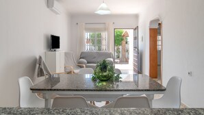 A dining area with a granite table, white chairs, a small plant, and a television on a cabinet. - Holiday Home 'Diego' with Private Garden and Wi-Fi (Vejer de la Frontera)