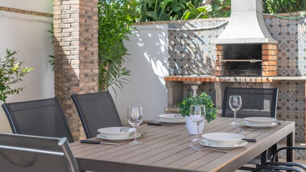 A dining table set with plates, glasses, and cutlery, surrounded by chairs, with a brick wall and a tiled oven in the background. - Holiday Home 'Diego' with Private Garden and Wi-Fi (Vejer de la Frontera)