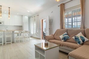 Ein modernes Wohnzimmer mit Glastisch, beiger Couch und weißen Stühlen.