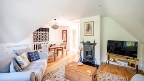 A living room with a sofa, TV, fireplace, and a dining area with a table and chairs. - Comfortable Cottage with Decking in Castle Cary (Castle Cary)