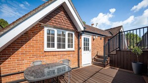 A brick house with a white door, a window with shutters, a wooden deck, and a metal fence. - Comfortable Cottage with Decking in Castle Cary (Castle Cary)