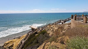 Un paseo marítimo con una escalera de madera que baja a la playa, un mirador y un área cercada con un banco.
