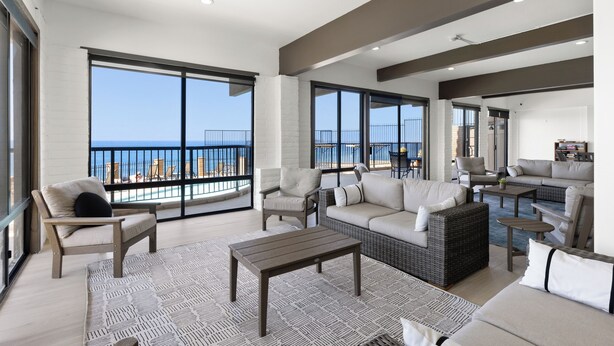 Amplia sala de estar con balcón con vistas al mar, amueblada con sofás, sillas y una mesa de centro.