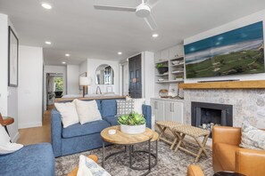 A living room with a blue sofa, a coffee table, a fireplace, and a television mounted on the wall. - Sunset Passage - Top floor corner unit with ocean views (Solana Beach)
