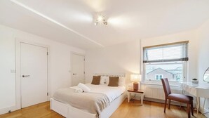 A bedroom with a bed, bedside table, lamp, chair, window, radiator, and a door. - Charming 1BR Apartment | Parking Included (Windsor)