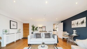 A modern living room with a white sofa, a coffee table, and a dining area with a table and chairs. - Charming 1BR Apartment | Parking Included (Windsor)