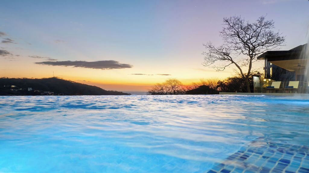 Une piscine avec vue sur un coucher de soleil et une colline en arrière-plan.