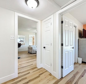 A hallway with wooden flooring, white doors, and a ceiling light fixture.