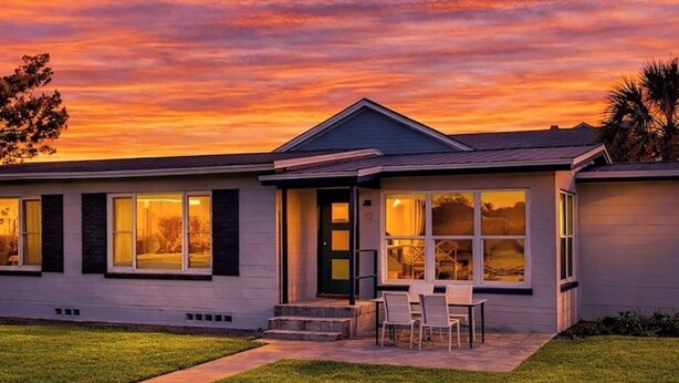 A modern two-story house with a flat roof, large windows, and a well-maintained lawn.