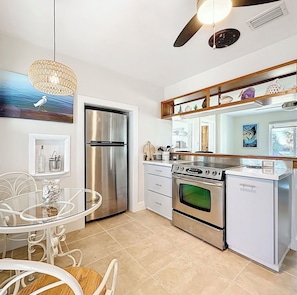 Una cocina moderna con un refrigerador de acero inoxidable, una estufa a gas y un horno empotrado. Hay una mesa de comedor con sillas, un ventilador de techo y una lámpara decorativa.