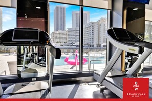 A gym with exercise equipment and a large window with a city view. - Modern 1BR · Bay View · Pool & Resort Access (Hallandale Beach)