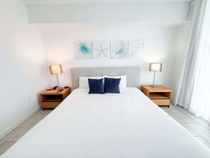 A large bed with two nightstands, each with a lamp, in a room with a simple, clean design. - City & Marina Views · 2BR Beachwalk Resort (Hallandale Beach)