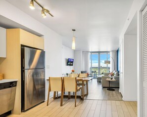 Une cuisine moderne équipée d’un réfrigérateur en acier inoxydable, d’une table à manger avec des chaises et d’un téléviseur fixé au mur.
