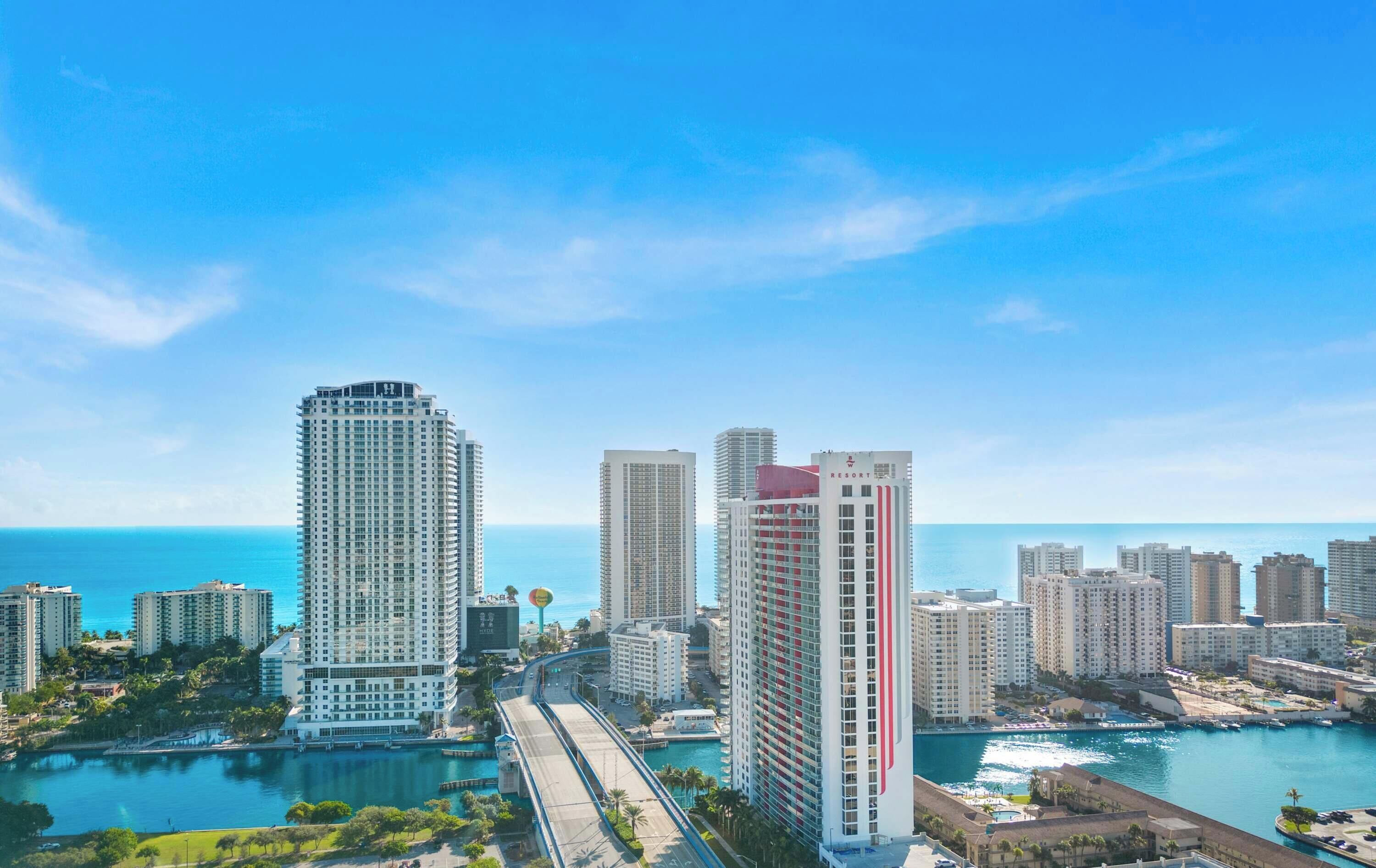 Un paisaje urbano costero con rascacielos, un puerto deportivo y un cielo azul despejado.