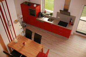A modern kitchen with red cabinets, a wooden dining table, and a view of the outdoors. - Holiday Home Jan Groen 8 (Wurster Nordseeküste)