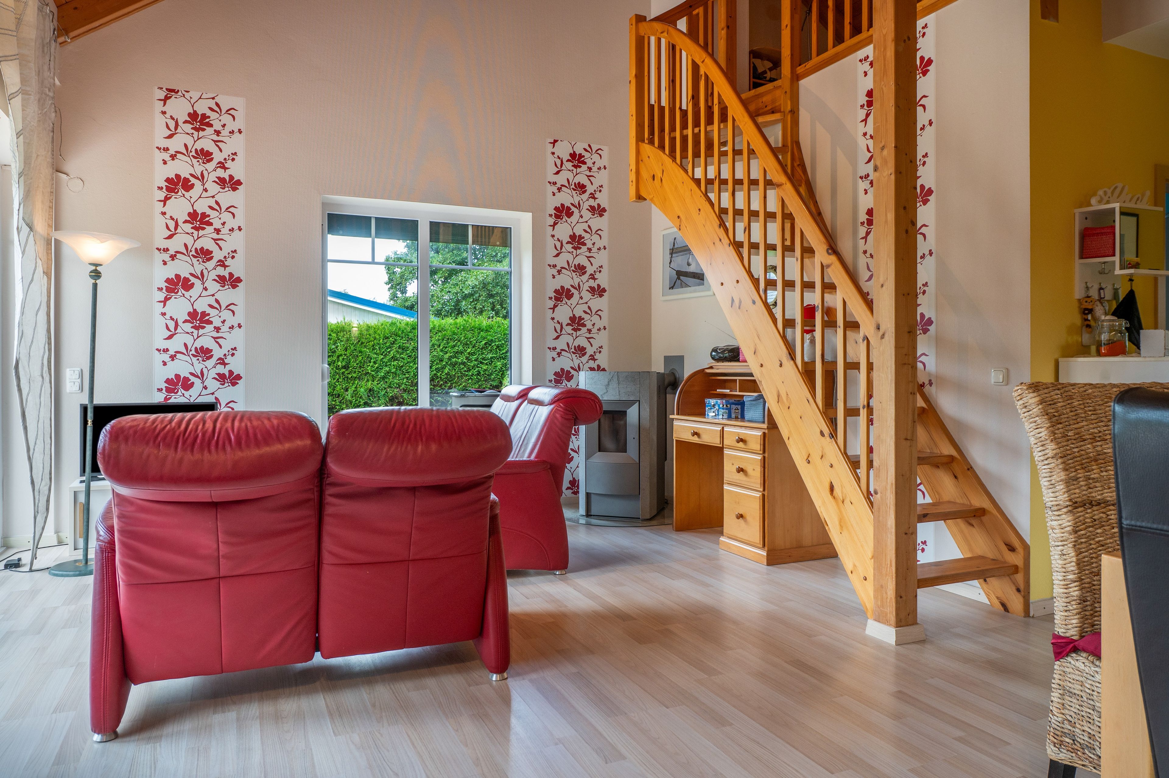Un salon avec un escalier en bois, des canapés rouges et une grande fenêtre donnant sur un paysage verdoyant.
