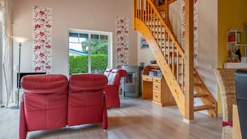 Un salon avec un escalier en bois, des canapés rouges et une grande fenêtre donnant sur un paysage verdoyant.
