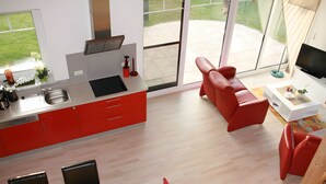 A modern kitchen with red cabinets, a dining area with a wooden table and chairs, and a red sofa. - Holiday Home Jan Groen 8 (Wurster Nordseeküste)