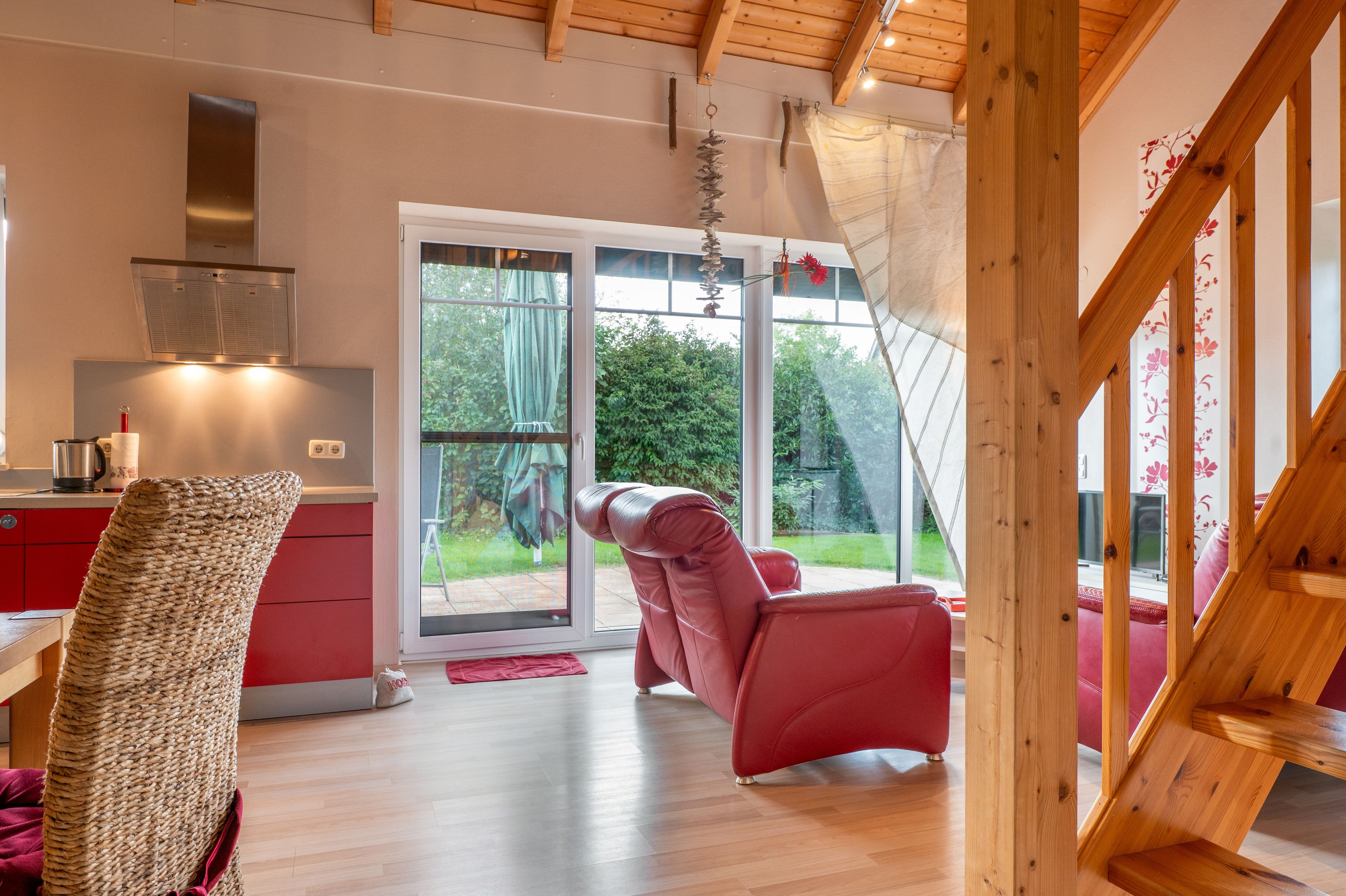 A modern kitchen with a red countertop, a stainless steel range hood, and a view of a garden through a sliding glass door.