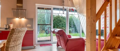 A modern kitchen with a red countertop, a stainless steel range hood, and a view of a garden through a sliding glass door.