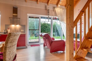 Een moderne keuken met een rode aanrecht, een roestvrijstalen afzuigkap en uitzicht op een tuin via een schuifdeur.