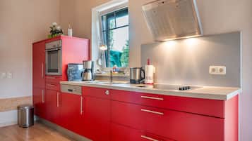 Una cocina moderna con armarios rojos, electrodomésticos de acero inoxidable y ventana con vistas a zonas verdes.