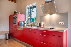 A modern kitchen with red cabinetry, stainless steel appliances, and a window overlooking greenery. - Holiday Home Jan Groen 8 (Wurster Nordseeküste)