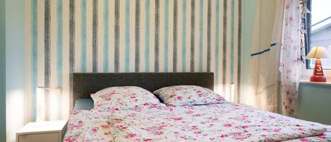 Una cama con ropa de cama floral, una pared a rayas y una ventana con cortinas.