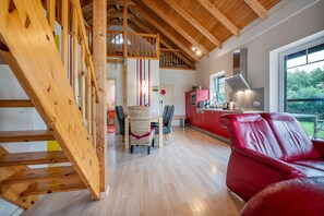 Un vaste espace de vie comprenant un canapé en cuir rouge, un escalier en bois et un coin cuisine avec des meubles de couleur rouge.