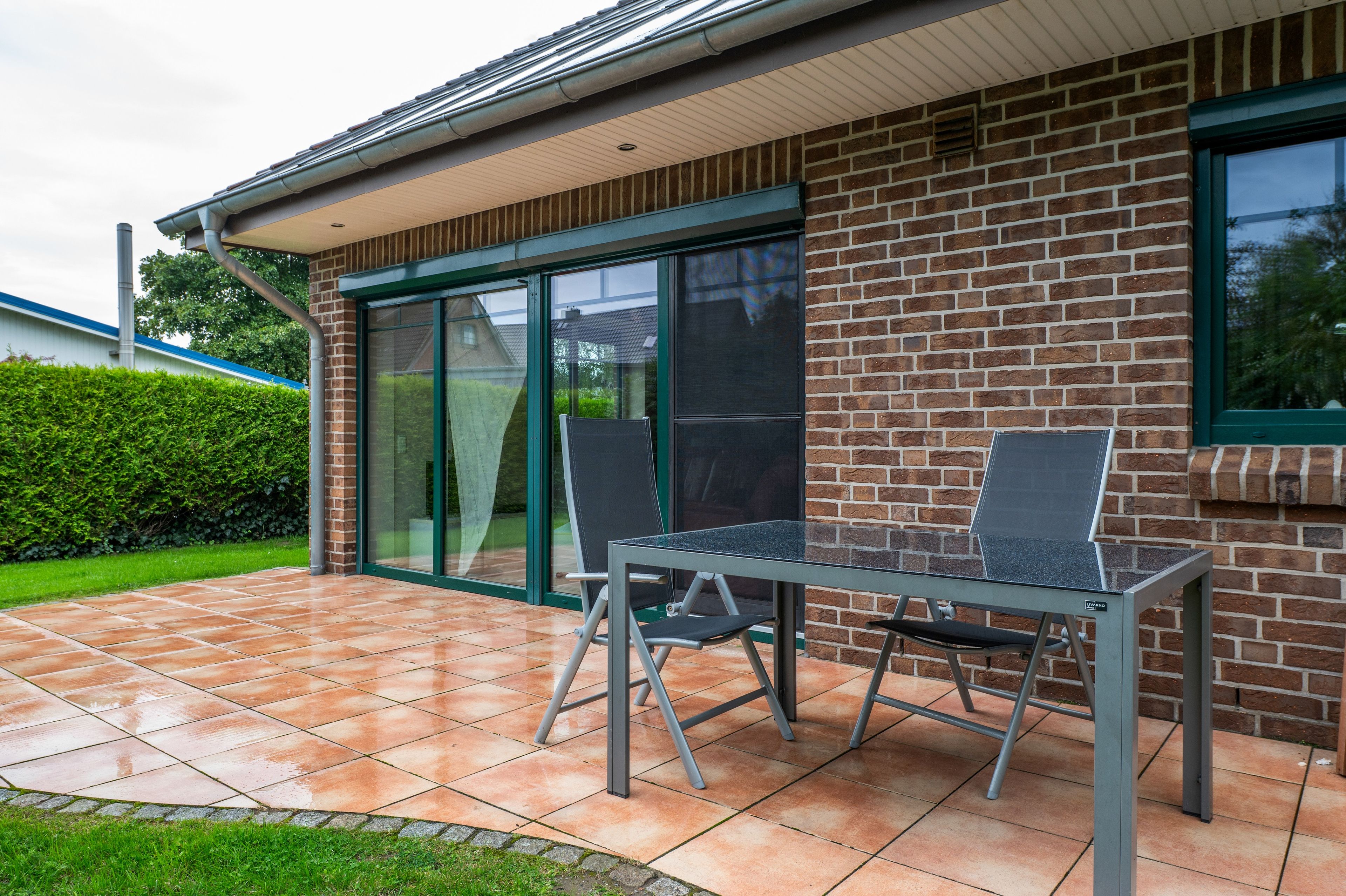 A patio with a table and chairs, a brick wall, and a glass door.