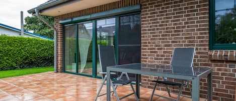 A patio with a table and chairs, a brick wall, and a glass door.