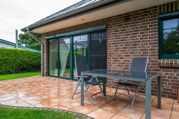 A patio with a table and chairs, a brick wall, and a glass door. - Holiday Home Jan Groen 8 (Wurster Nordseeküste)