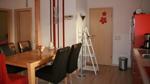 A dining area with a wooden table and chairs, a white floor lamp, and a red flower decoration on the wall. - Holiday Home Jan Groen 8 (Wurster Nordseeküste)