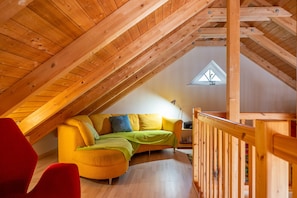 A cozy attic room with a wooden ceiling, a yellow sofa with green and blue cushions, and a red chair. - Holiday Home Jan Groen 8 (Wurster Nordseeküste)
