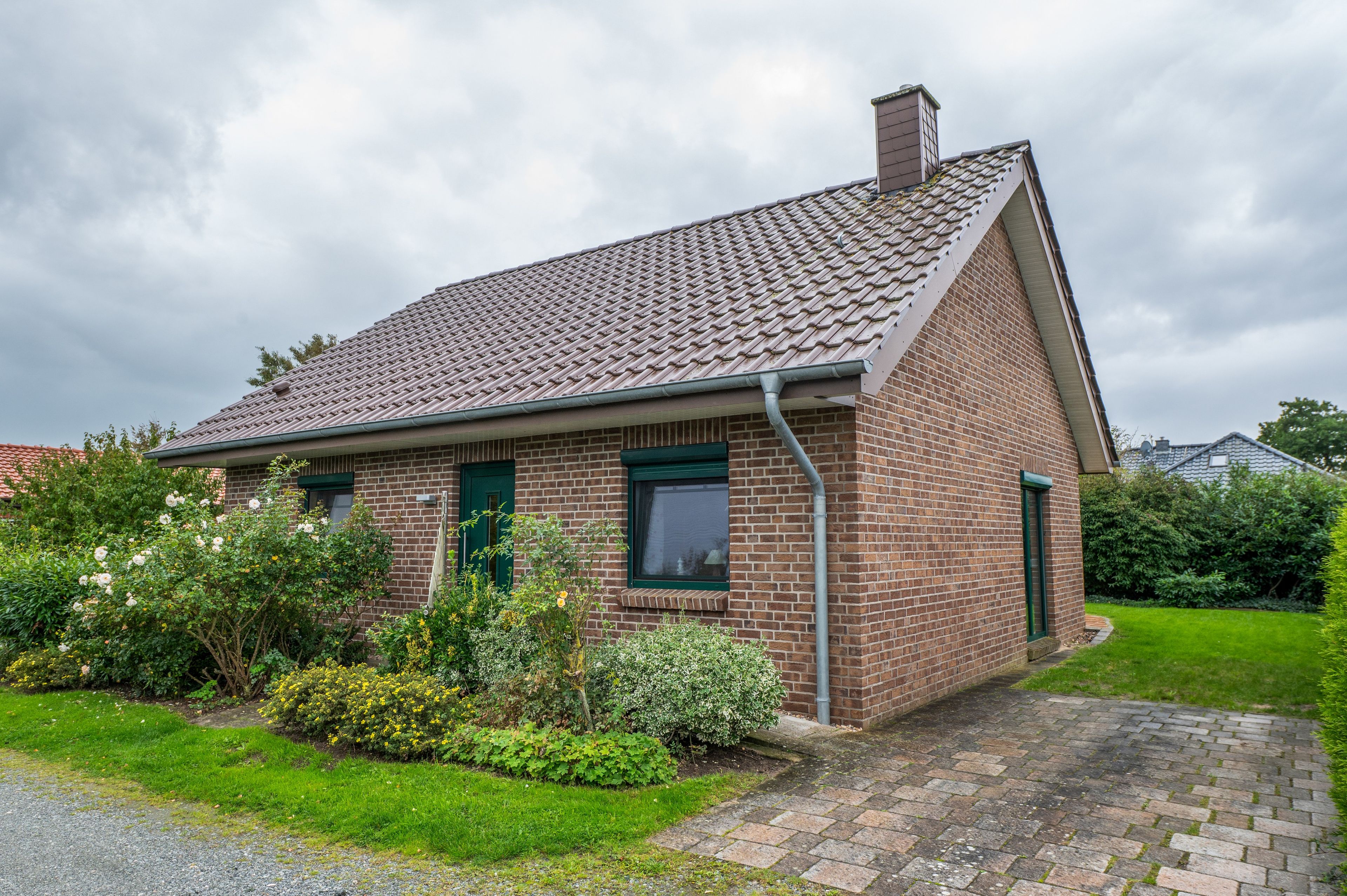 Ein einstöckiges Haus aus Backstein mit Ziegeldach, einer Haustür und einem kleinen Garten mit verschiedenen Pflanzen und Blumen.