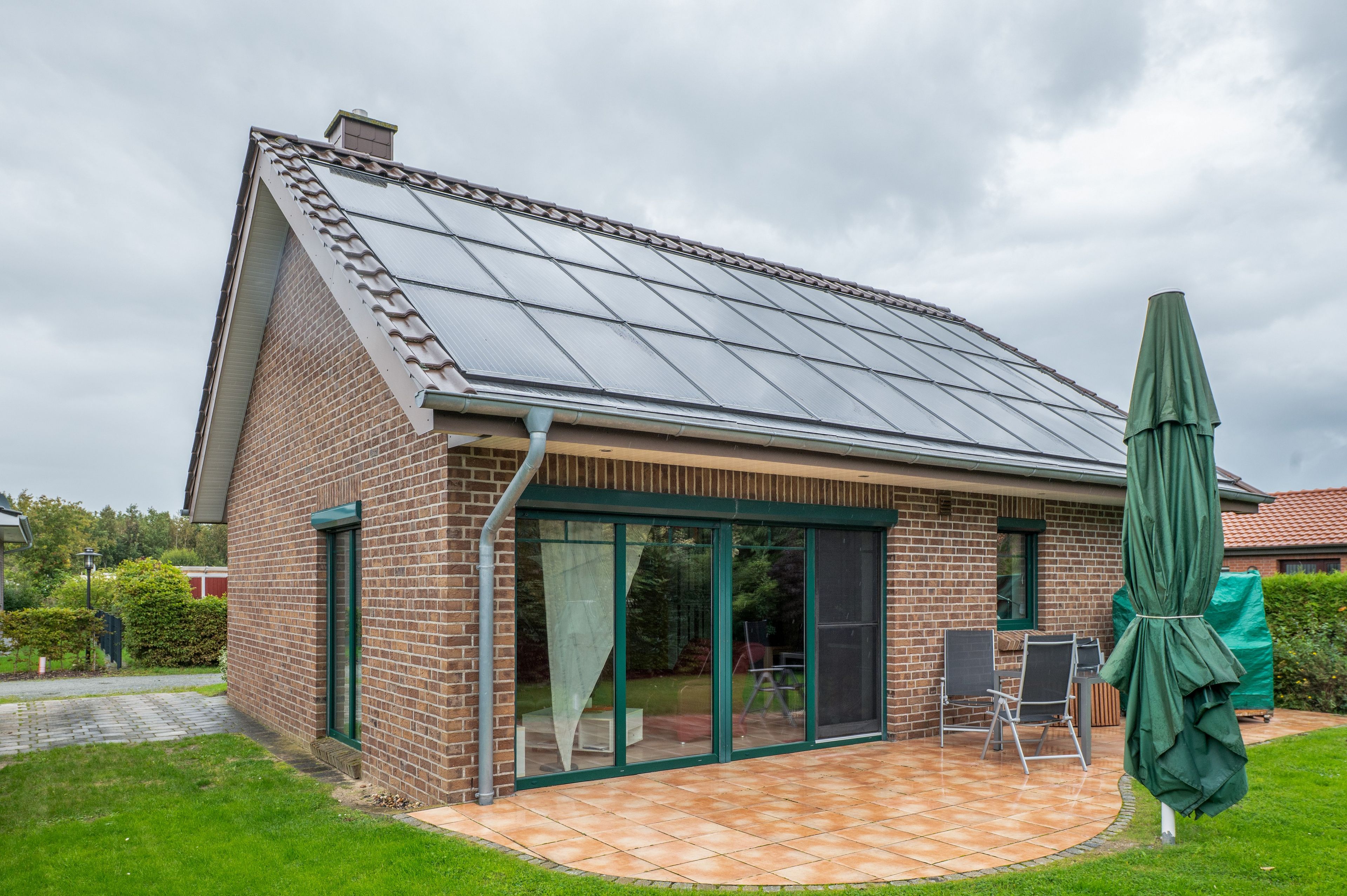 Ein Haus mit Ziegelaußenwand, einer gefliesten Terrasse und einem grünen Sonnenschirm.