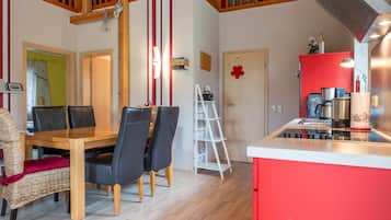 Une cuisine moderne avec un meuble rouge, une table à manger en bois avec des chaises et une échelle blanche.